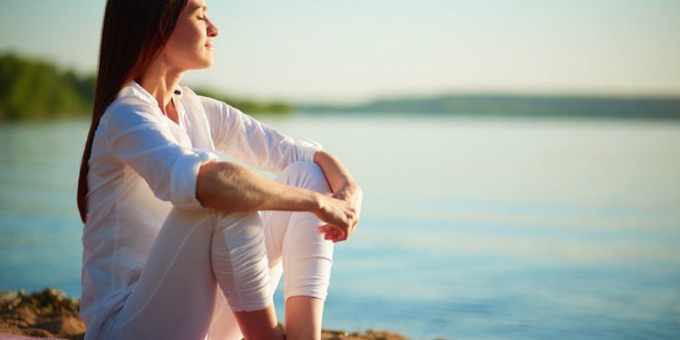 Side view of serene woman sitting on sandy beach against blue sky outdoors
