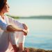 Side view of serene woman sitting on sandy beach against blue sky outdoors